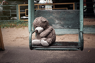 Wet miserable teddy bear left behind on a swing