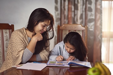 Shot of a mother helping her daughter with school work at home
